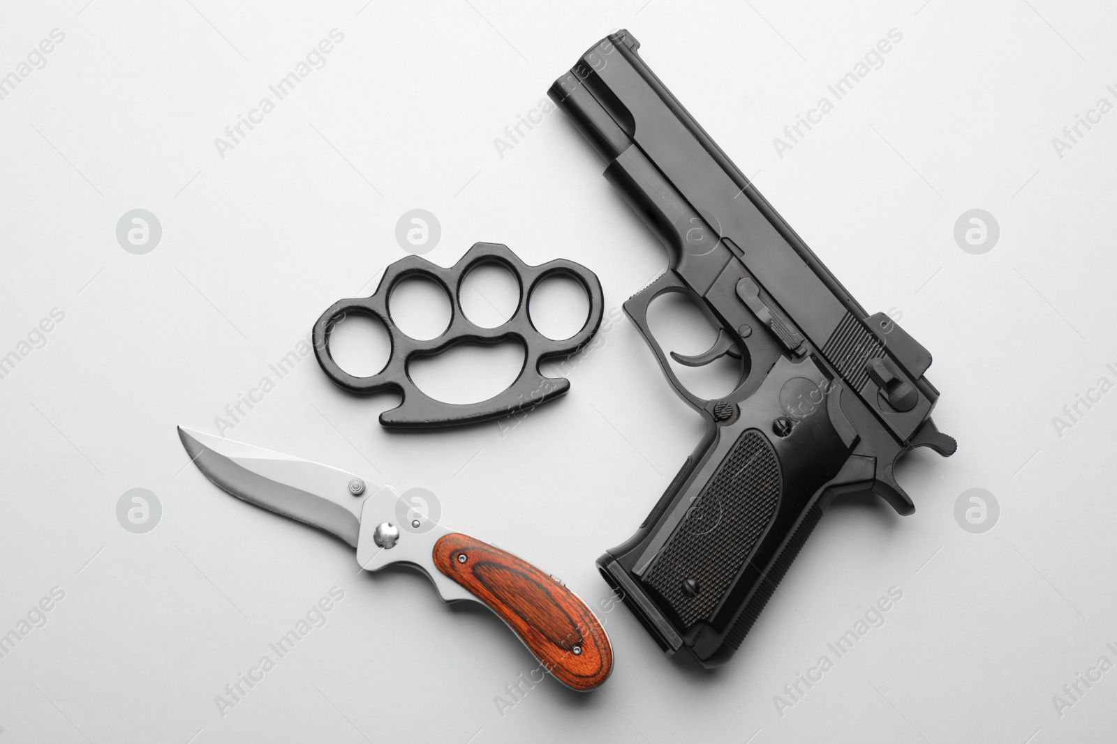 Photo of Black brass knuckles, gun and knife on white background, flat lay