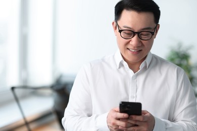Photo of Portrait of smiling businessman with smartphone in office. Space for text