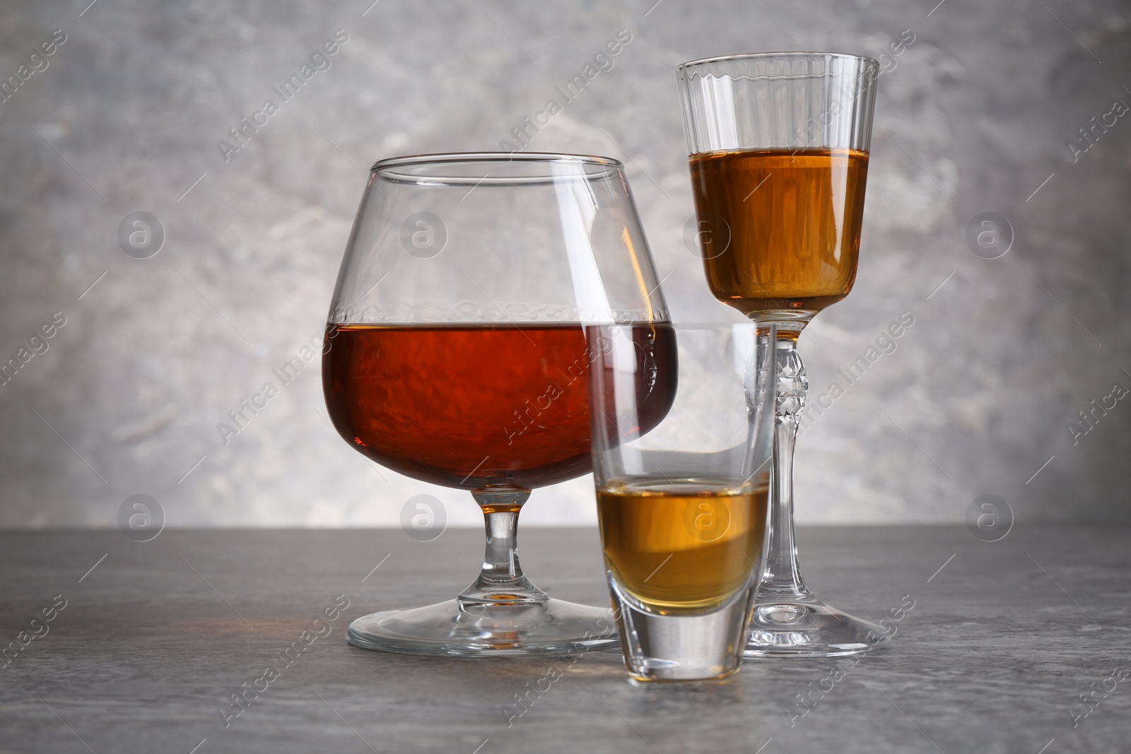 Photo of Different liqueurs in glasses on grey textured table, closeup