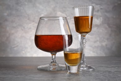 Photo of Different liqueurs in glasses on grey textured table, closeup