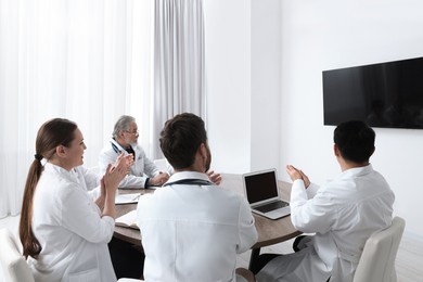 Photo of Team of doctors watching presentation on tv screen in room. Medical conference