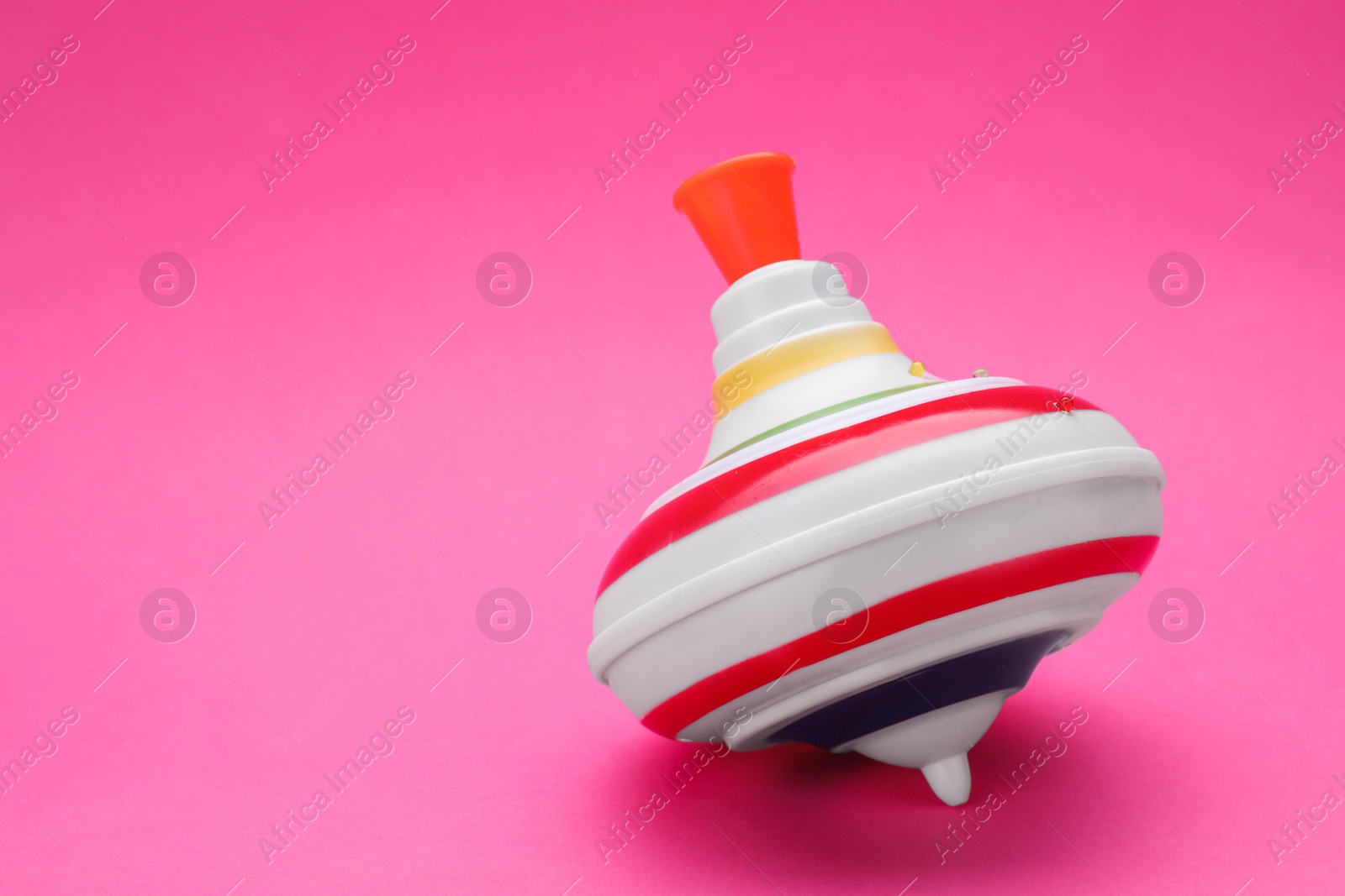 Photo of One bright spinning top on pink background, space for text. Toy whirligig