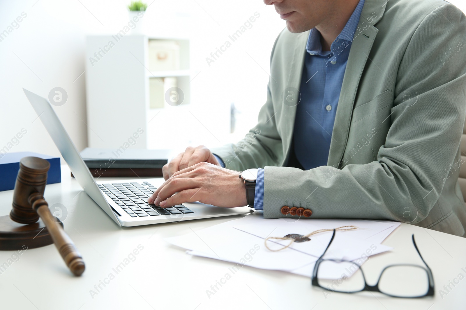 Photo of Notary working with laptop and judge gavel on table, closeup. Law and justice concept