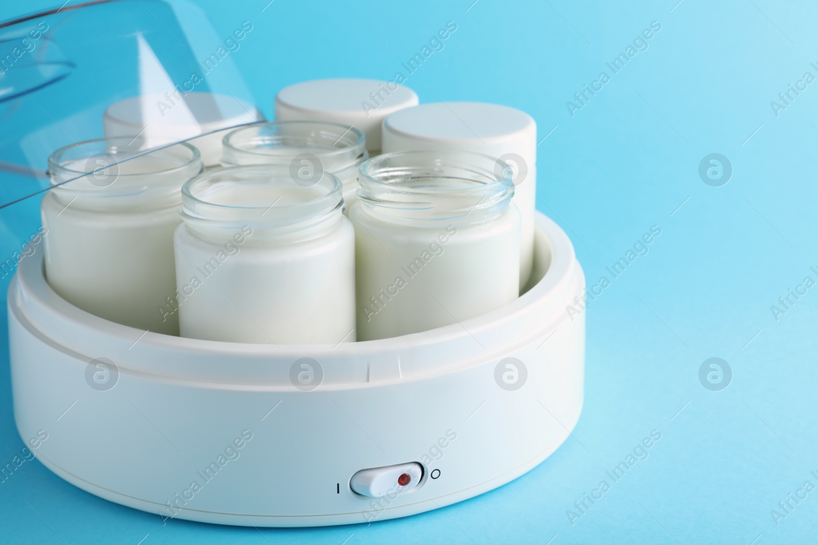 Photo of Modern yogurt maker with full jars on light blue background