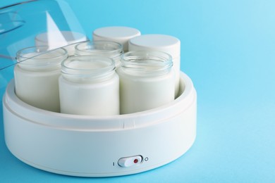 Photo of Modern yogurt maker with full jars on light blue background