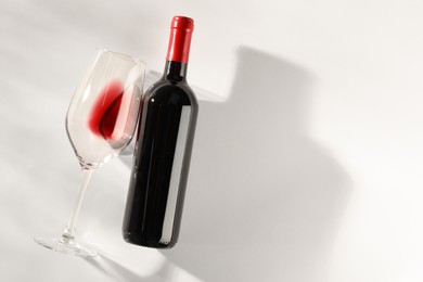Photo of Bottle of expensive red wine and wineglass on light background, top view. Space for text