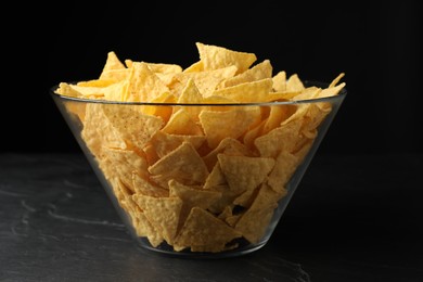 Photo of Glass bowl with tortilla chips (nachos) on black table against dark background