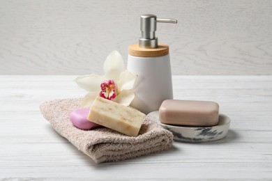 Photo of Soap bars, dispenser and terry towel on white wooden table