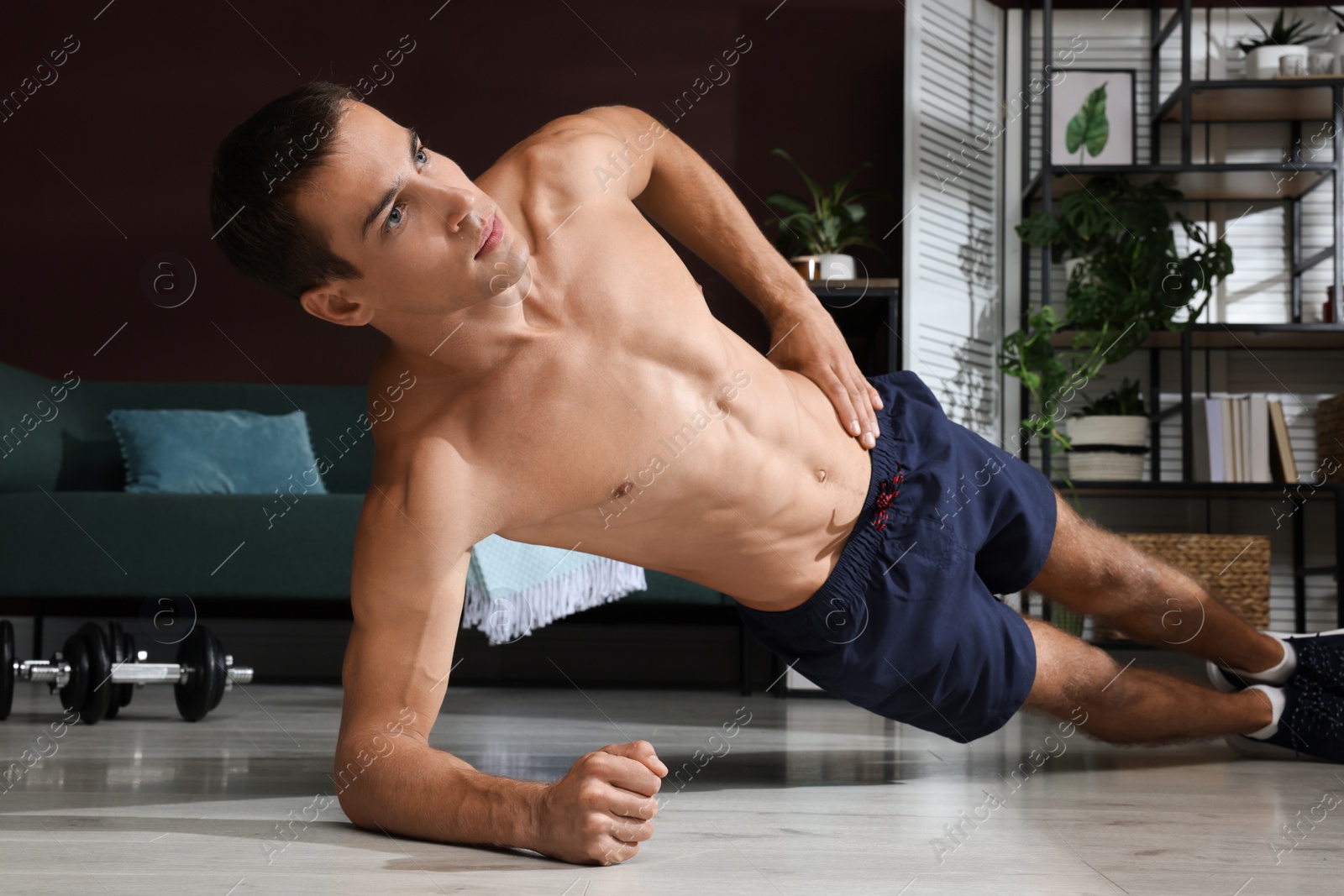 Photo of Handsome man doing side plank exercise on floor at home