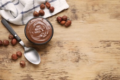 Photo of Bowl with delicious chocolate paste and nuts on wooden table, flat lay. Space for text