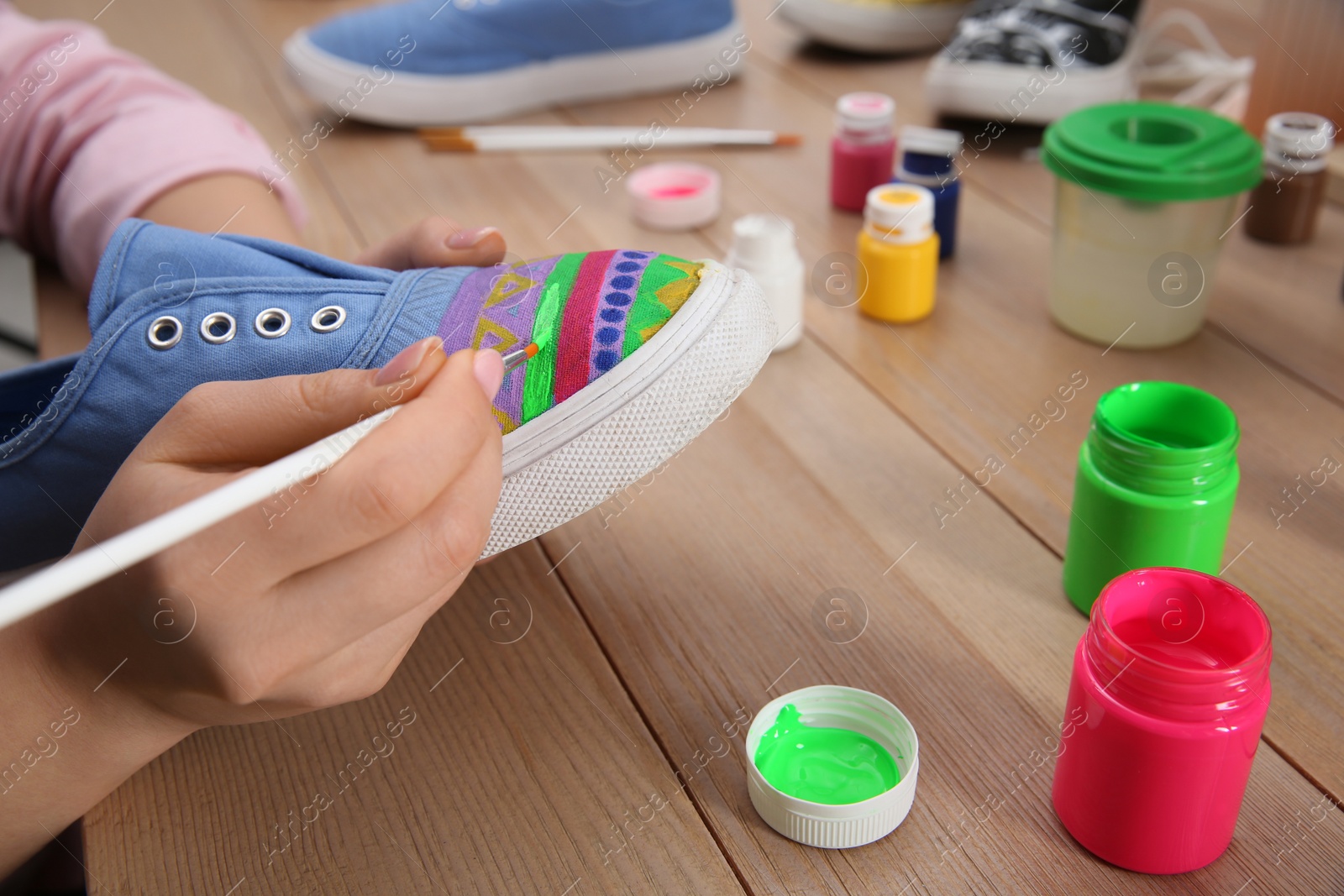 Photo of Woman painting on sneaker at wooden table, closeup. Customized shoes