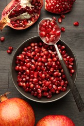 Photo of Tasty ripe pomegranates and grains on dark wooden table, top view