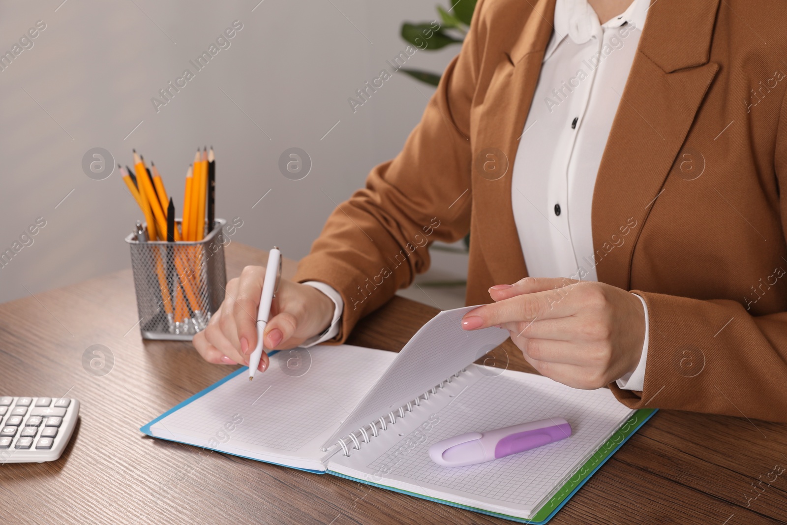 Photo of Woman taking notes at wooden table indoors, closeup