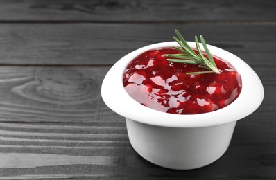 Photo of Fresh cranberry sauce in bowl and rosemary on black wooden table, closeup. Space for text