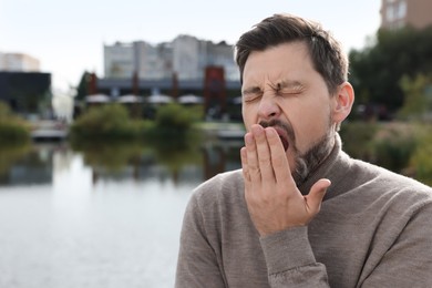 Photo of Sleepy man yawning near river outdoors. Space for text