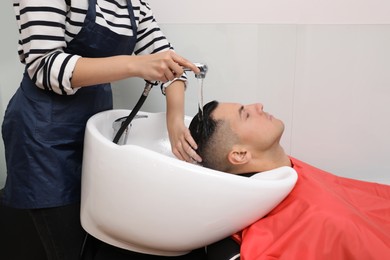 Photo of Professional hairdresser washing client's hair at sink in salon, closeup