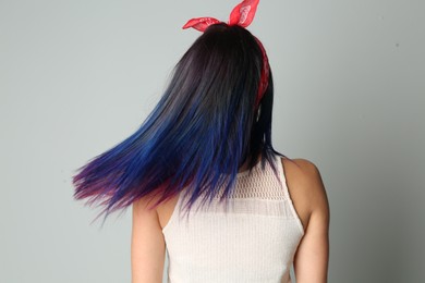 Photo of Young woman with bright dyed hair on grey background, back view