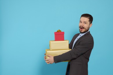 Emotional man in suit with gifts on light blue background. Space for text