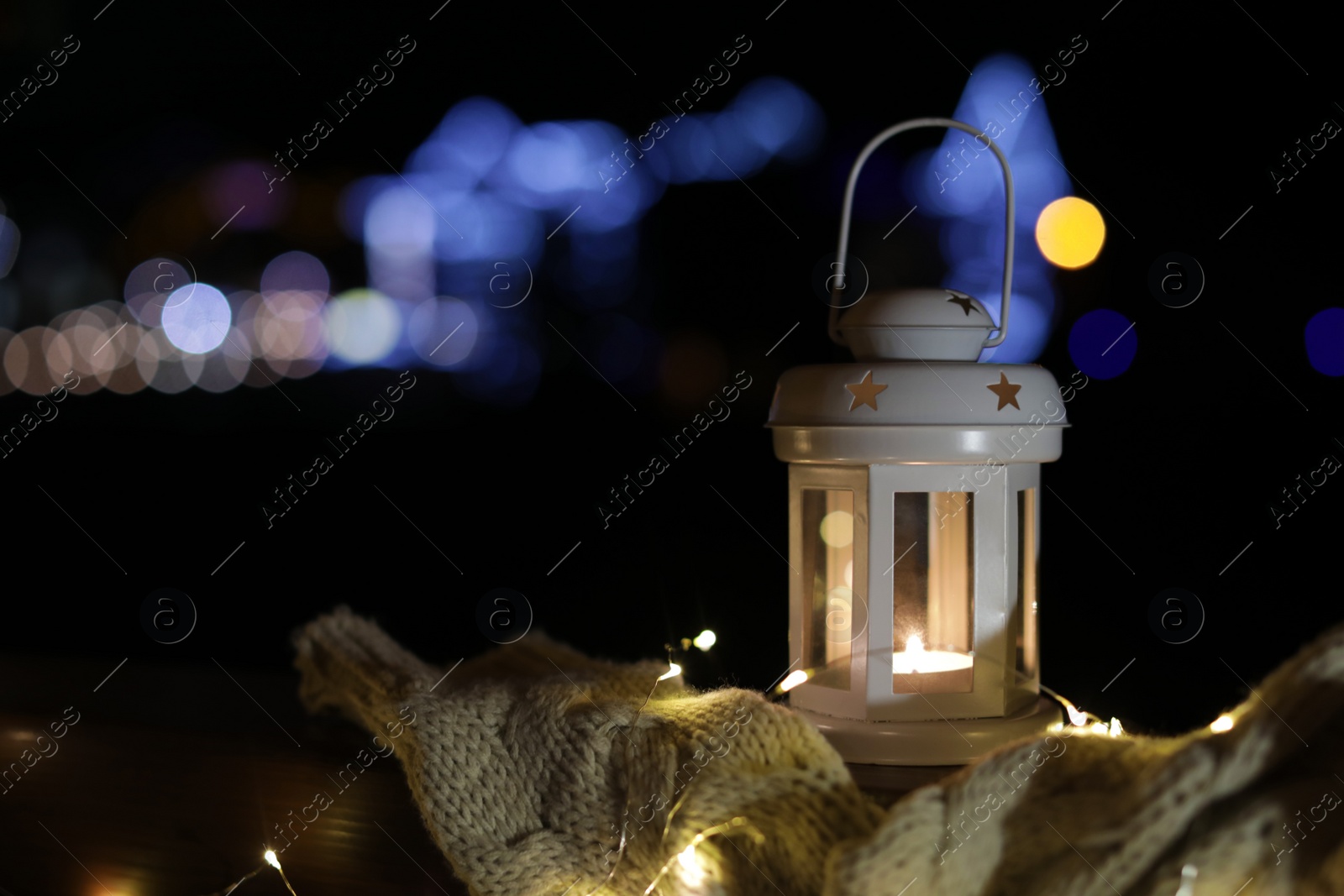 Photo of Lantern, sweater and Christmas lights outdoors on winter night. Space for text