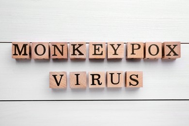 Photo of Words Monkeypox Virus made of cubes on white wooden table, flat lay