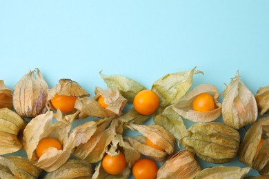 Photo of Ripe physalis fruits with calyxes on light blue background, flat lay. Space for text