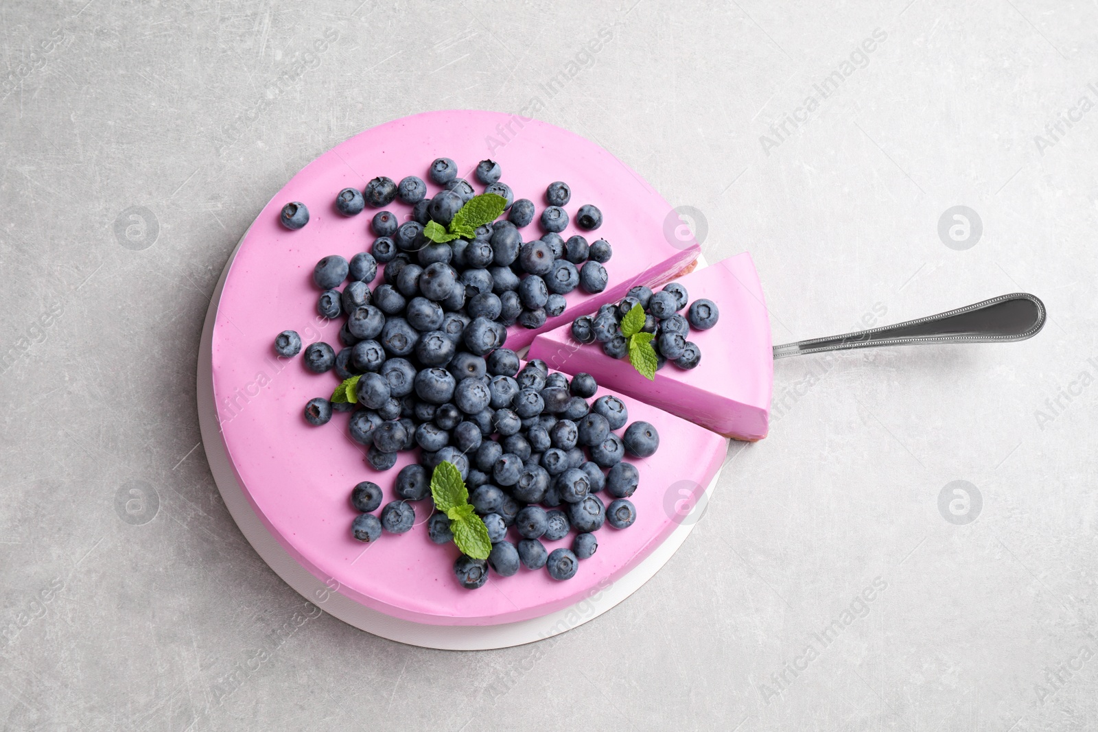 Photo of Cut tasty blueberry cake and shovel on light grey table, top view