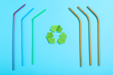 Recycling symbol, plastic and metal drinking straws on light blue background, flat lay