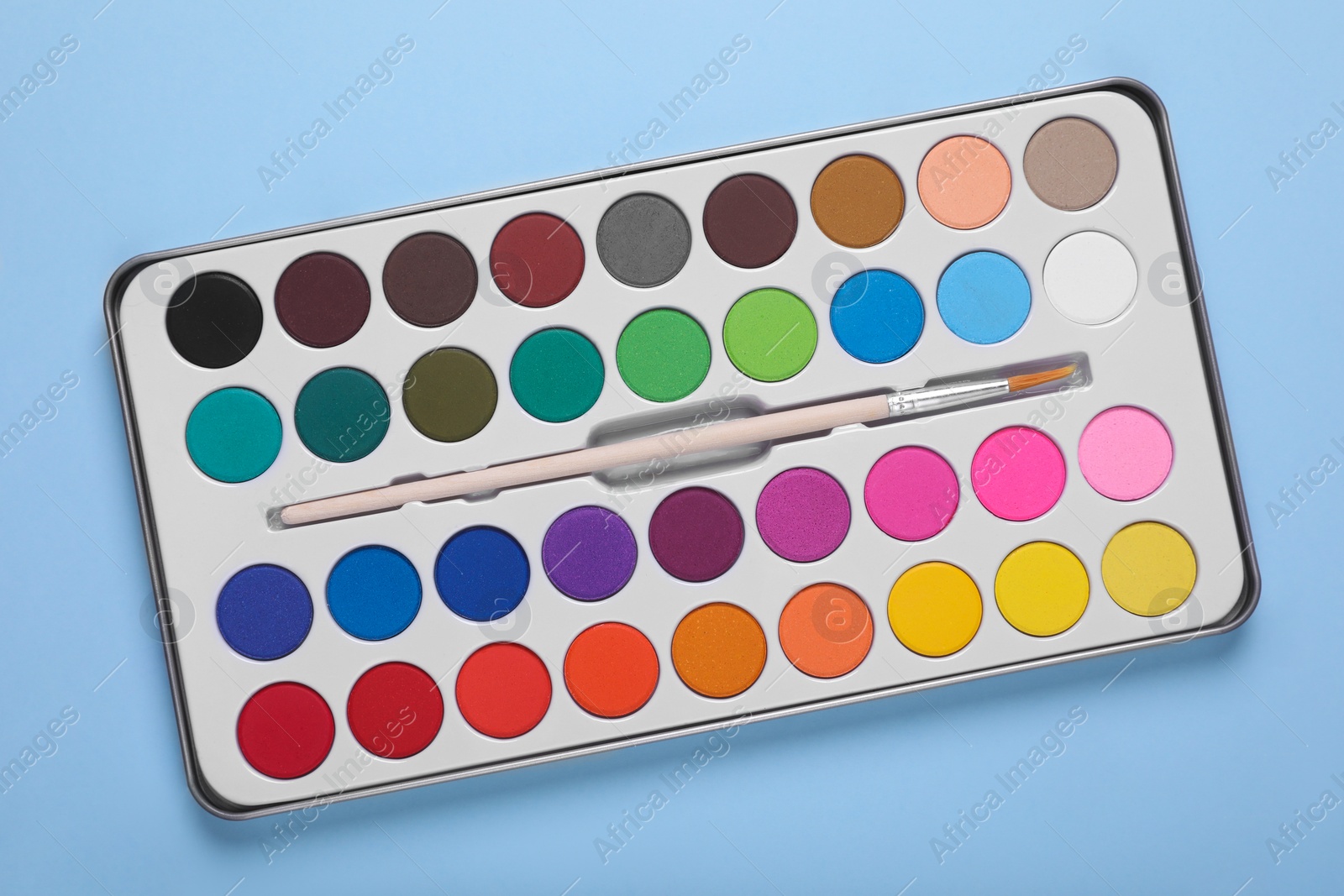 Photo of Watercolor palette with brush on light blue background, top view