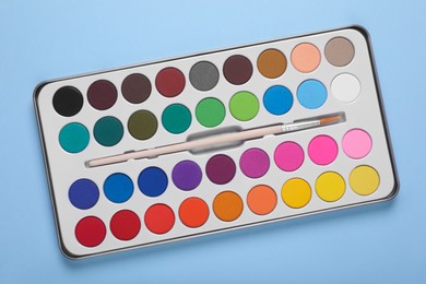 Photo of Watercolor palette with brush on light blue background, top view