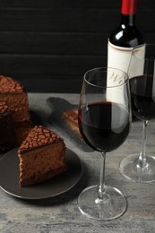 Photo of Delicious chocolate truffle cake and red wine on grey textured table