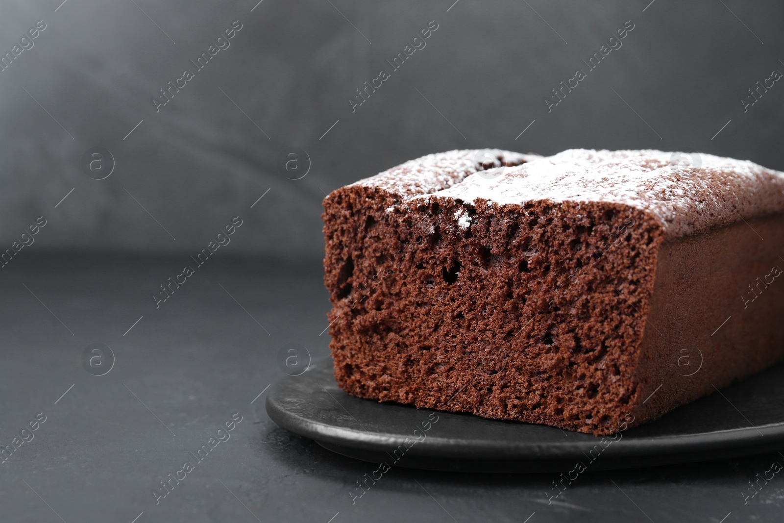 Photo of Tasty chocolate sponge cake with powdered sugar on black table, closeup. Space for text