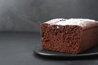 Tasty chocolate sponge cake with powdered sugar on black table, closeup. Space for text