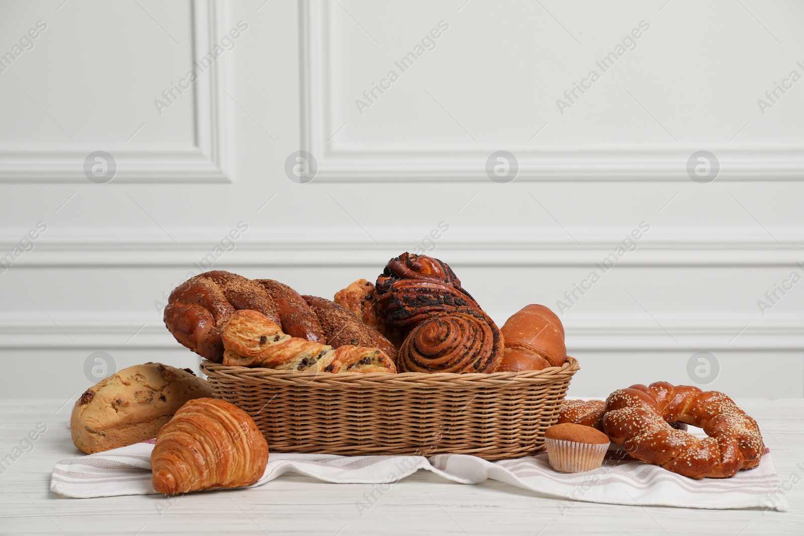 Photo of Wicker basket with different tasty freshly baked pastries on white wooden table, space for text