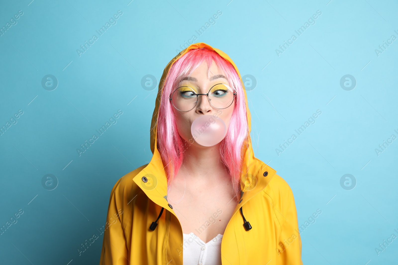 Photo of Fashionable young woman in pink wig with bright makeup blowing bubblegum on yellow background