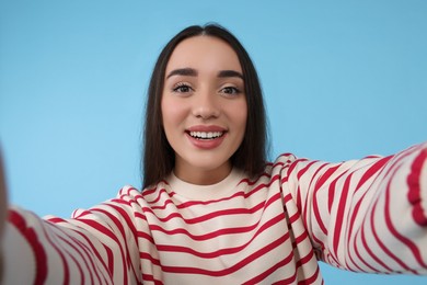 Smiling young woman taking selfie on light blue background