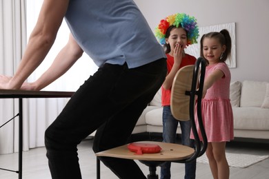 Photo of Cute little children putting whoopee cushion on father's chair while he sitting down at home, closeup