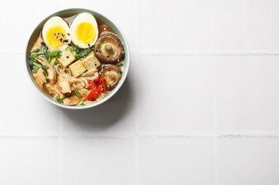 Photo of Noodle soup. Bowl of delicious ramen on white tiled table, top view. Space for text