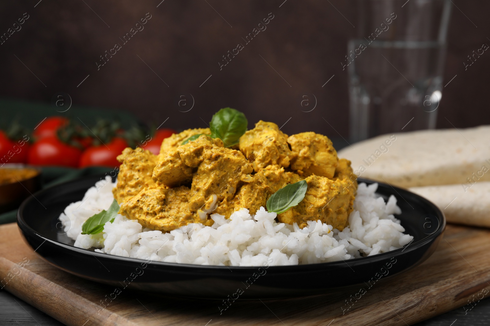 Photo of Delicious rice and chicken with curry sauce on wooden board, closeup