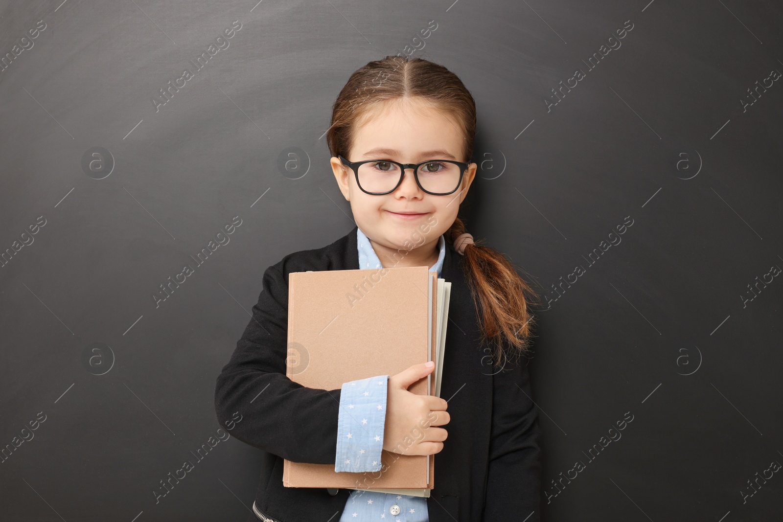 Photo of Happy little school child with books near chalkboard