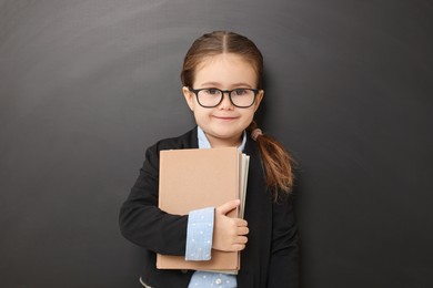 Photo of Happy little school child with books near chalkboard