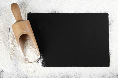 Photo of Frame made with flour near scoop on black table, flat lay. Space for text