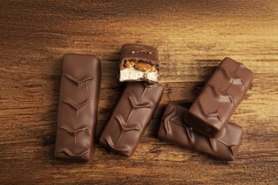 Photo of Chocolate bars with caramel, nuts and nougat on wooden table, flat lay