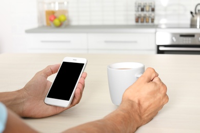 Photo of Man with modern mobile phone at table indoors, closeup