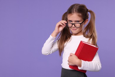 Photo of Cute schoolgirl with book on violet background. Space for text