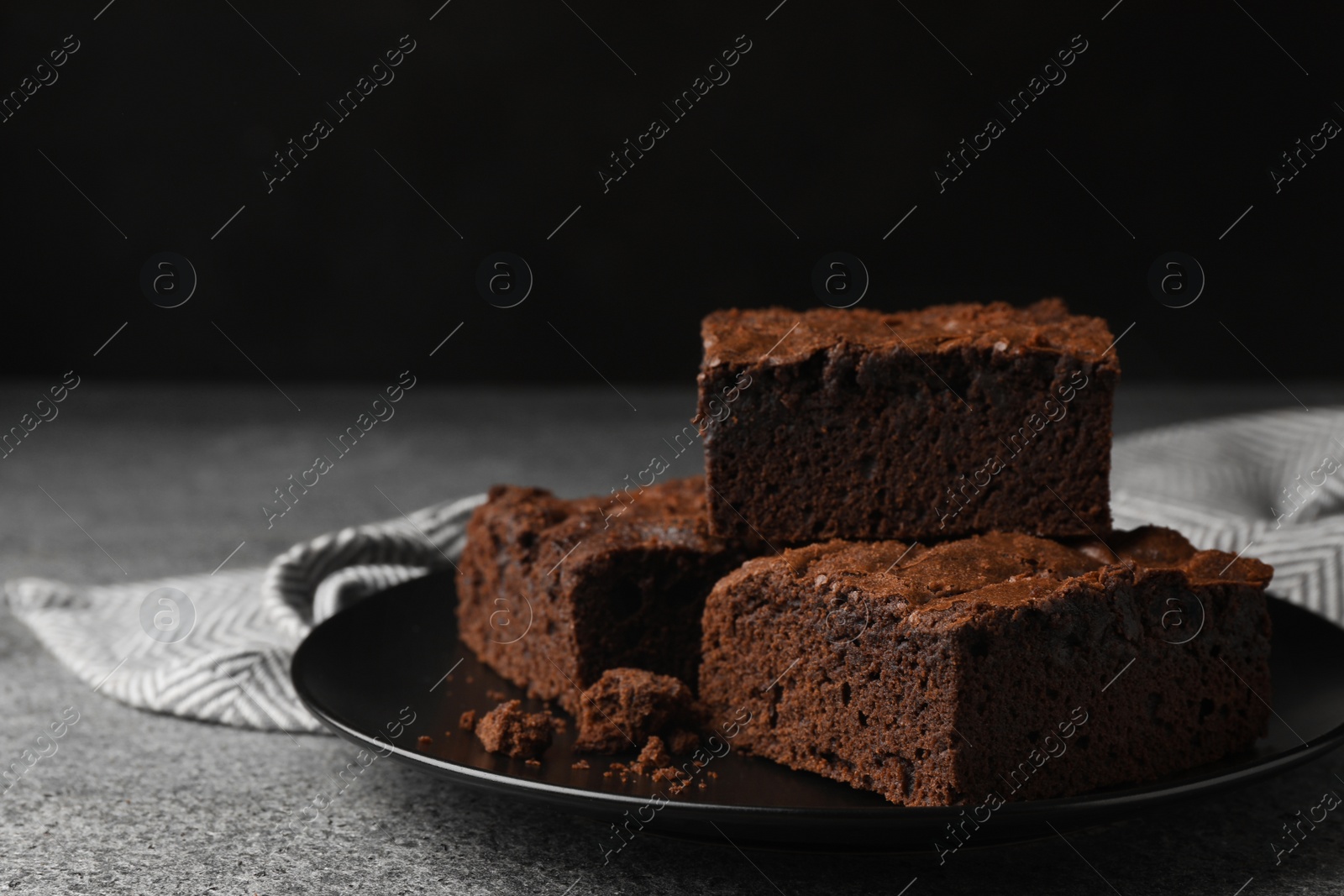 Photo of Plate with fresh brownies on grey table against black background, space for text. Delicious chocolate pie