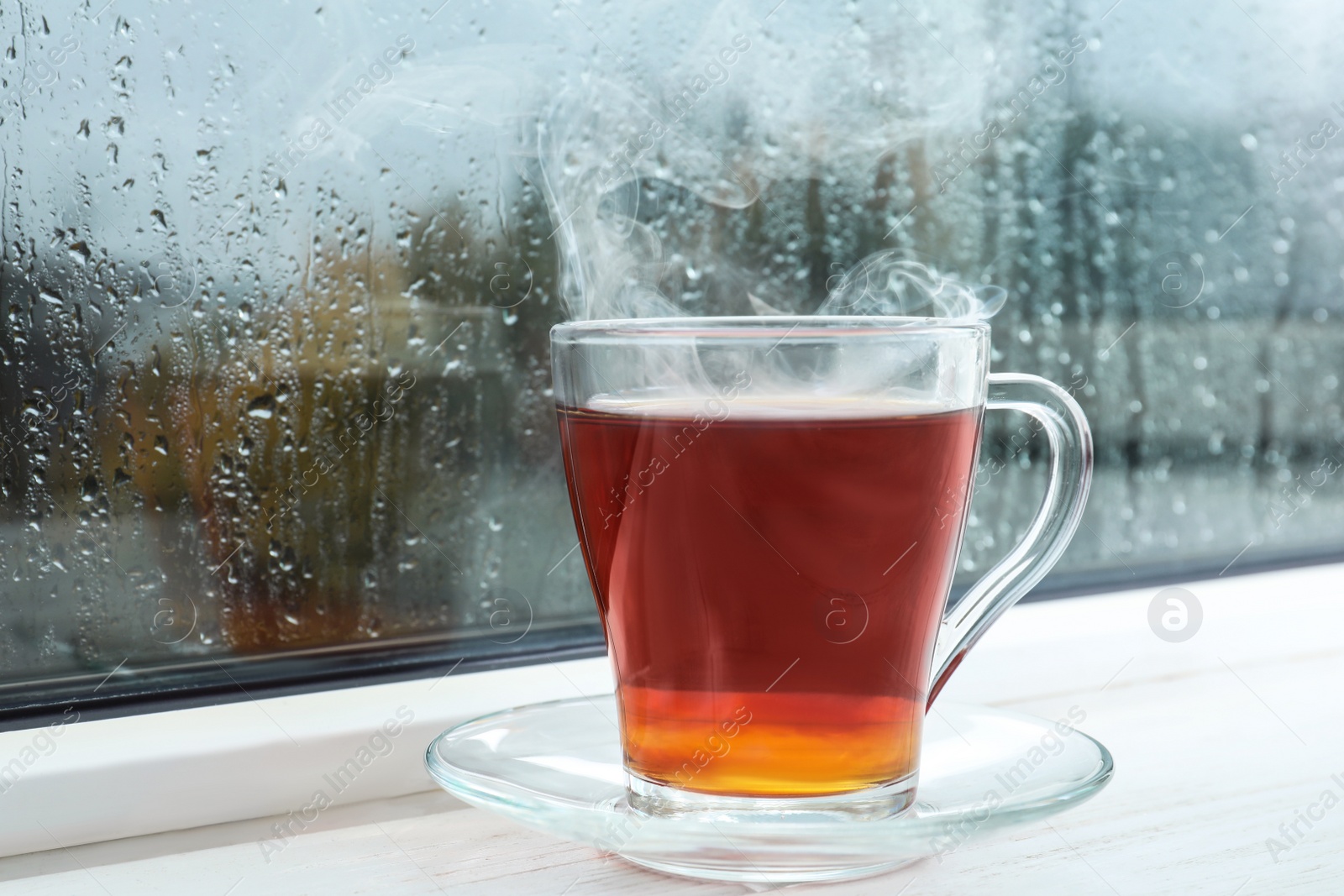 Photo of Glass cup of tea on windowsill. Rainy weather