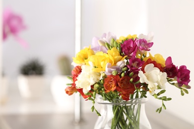 Photo of Vase with bright spring freesia flowers on table. Space for text