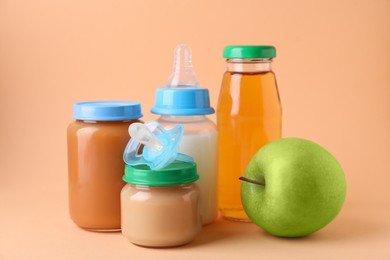 Photo of Healthy baby food, juice, milk, apple and pacifier on pale orange background
