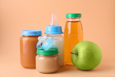 Healthy baby food, juice, milk, apple and pacifier on pale orange background