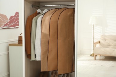 Photo of Garment bags with clothes on rack in wardrobe indoors